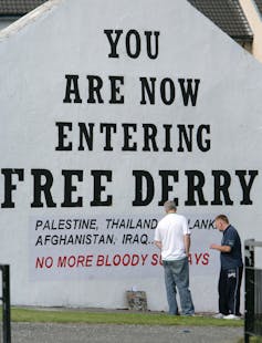 A building painted with the words You are now entering Free Derry, and a sign underneath reading Palestine Thailand Sri Lanka Afghanistan Iraq, No more bloody sundays.