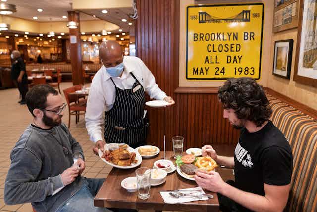 A waiter sets food on a table for two diners at a restaurant in New York