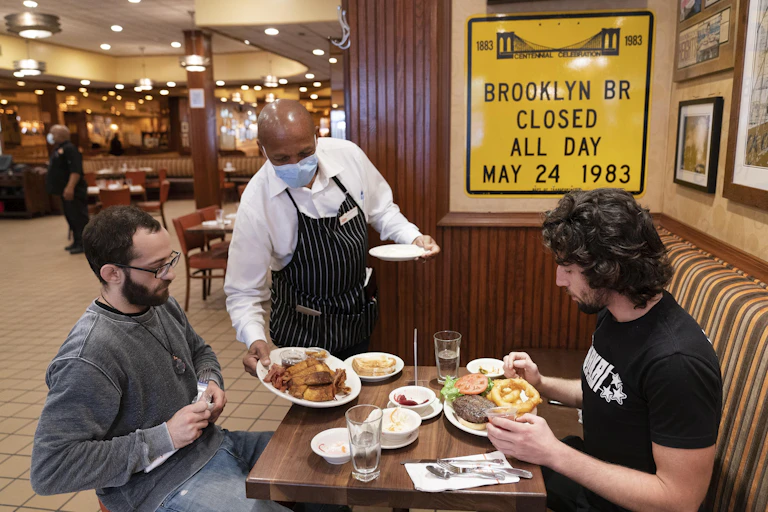 A waiter sets food on a table for two diners at a restaurant in New York