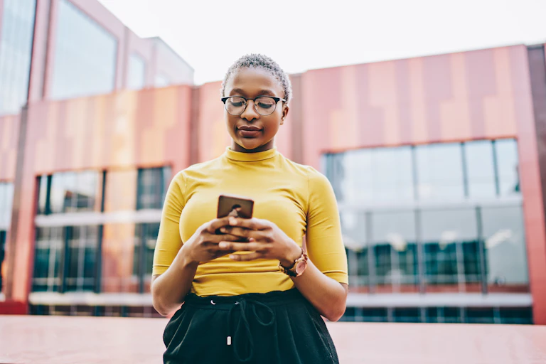 Black woman standing in front of building look at phone.