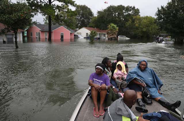 A family in a boat on a flooded street with water half-way up houses behind them