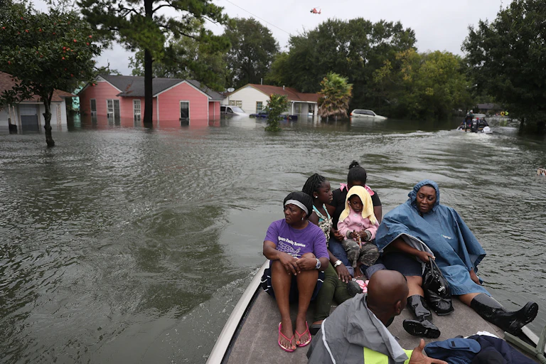 A family in a boat on a flooded street with water half-way up houses behind them