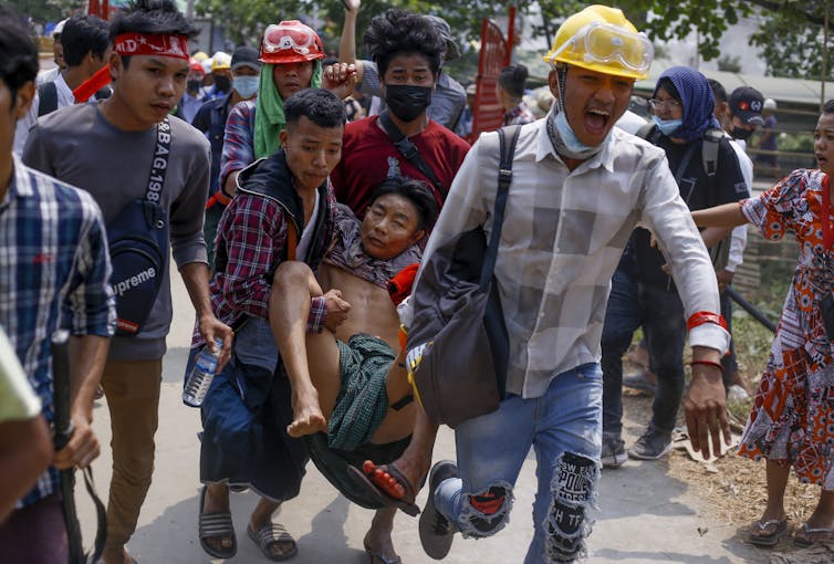 Anti-coup protesters carry an injured man.