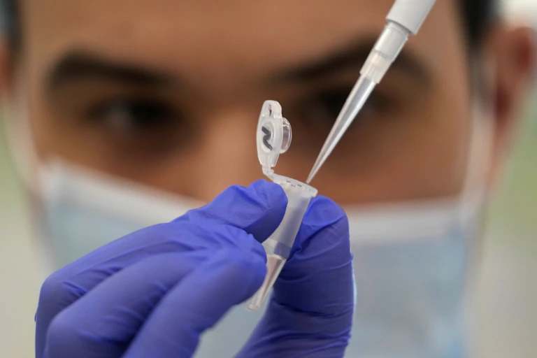 A scientist is seen holding a thin tube in gloved hands.
