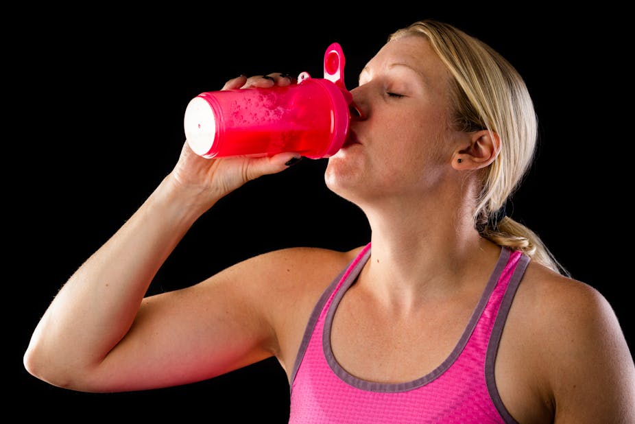A woman wearing workout clothes drinks a pre-workout supplement shake.