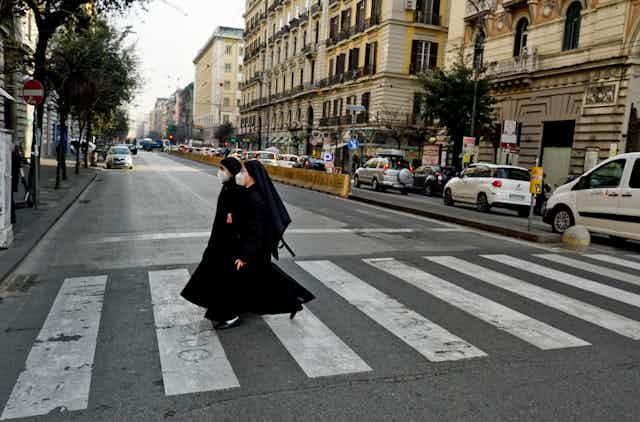 Two nuns wearing face masks crossing a street