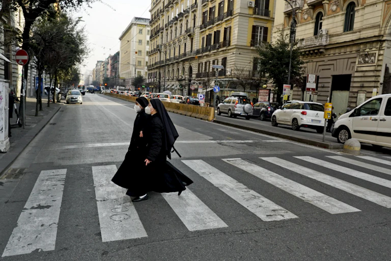 Two nuns wearing face masks crossing a street