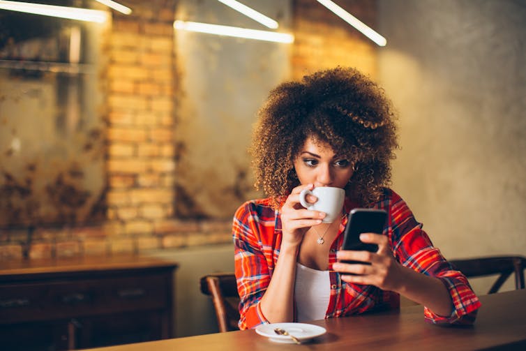 A woman drinking a cup of coffee looks at her smartphone.