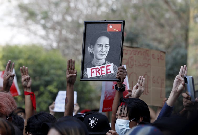 Group of protestors making three-fingered salutes and holiding picture of Aung San Su Kyi with the word 'free'