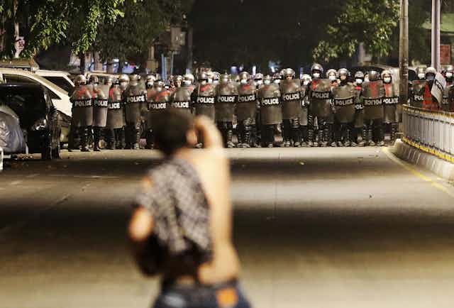 Protestor faces line of riot police on a road.
