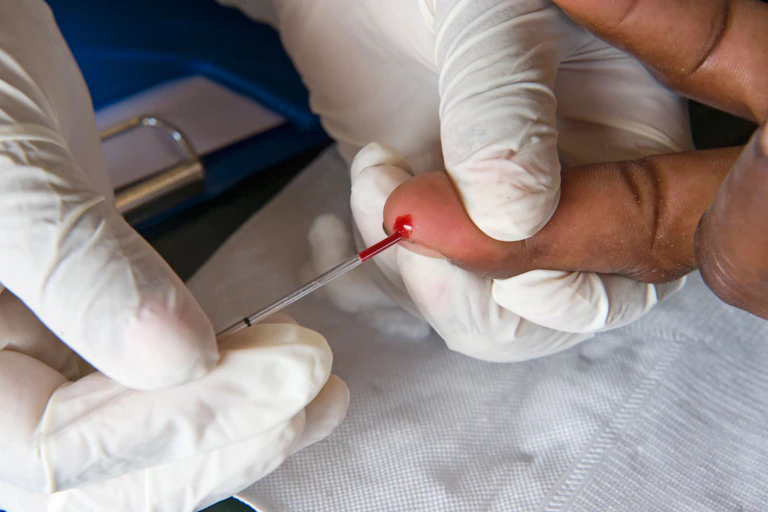 Gloved hand holding a pricked finger