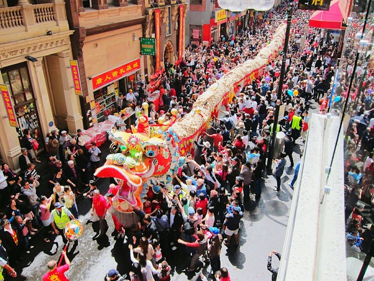 People dancing on streets while carrying a large cutout of a dragon during the Chinese New Year.