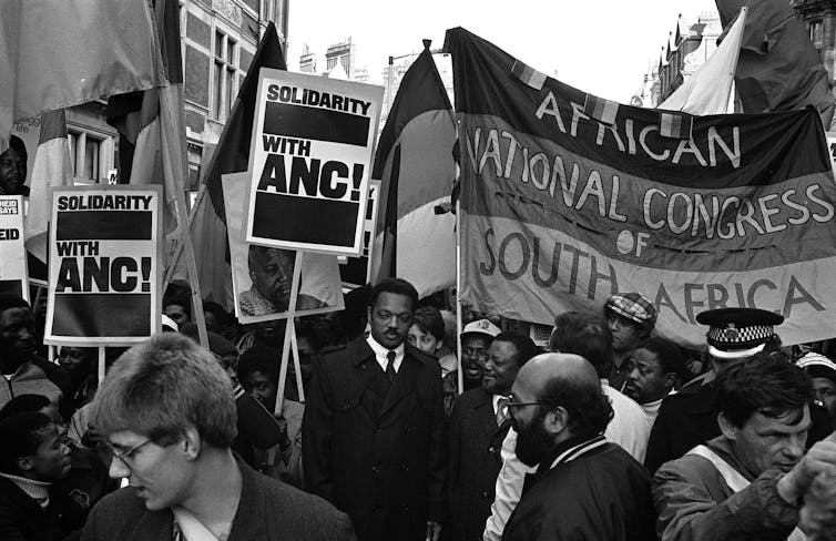 A Black man is marching with a crowd of protestors during an anti-apartheid demonstration.