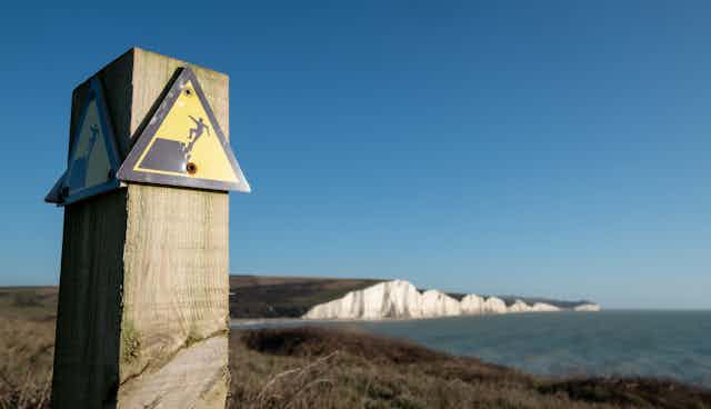 Cliff collapse warning sign with sea cliffs in background