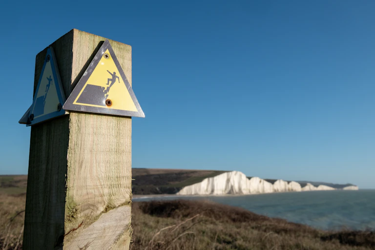 Cliff collapse warning sign with sea cliffs in background