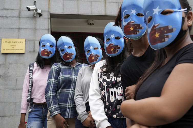 People standing in a line wearing blue masks with red hands painted across the mouth area