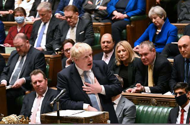 Boris Johnson placing his hand on his heart as he speaks in the House of Commons. Former prime minister Theresa May looks on in the background.