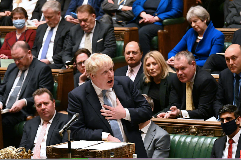 Boris Johnson placing his hand on his heart as he speaks in the House of Commons. Former prime minister Theresa May looks on in the background.