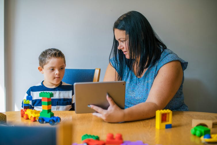 Mother shows son something on a tablet, while playing with blocks on the table.