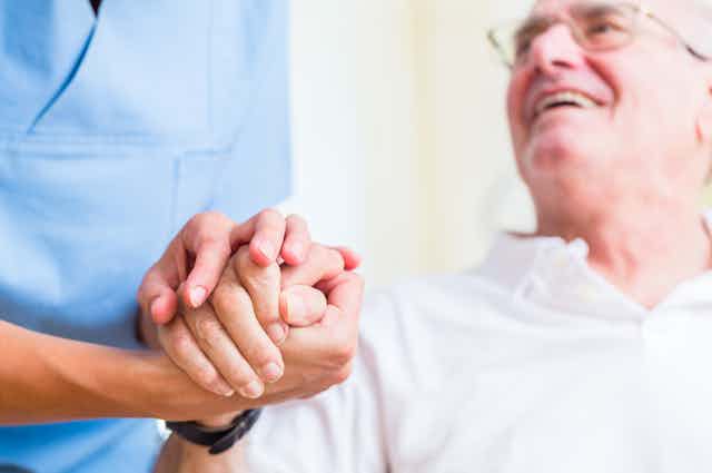 older man holds carer's hand