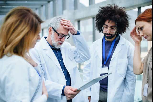 worried-looking researchers put hands to their heads as they discuss results