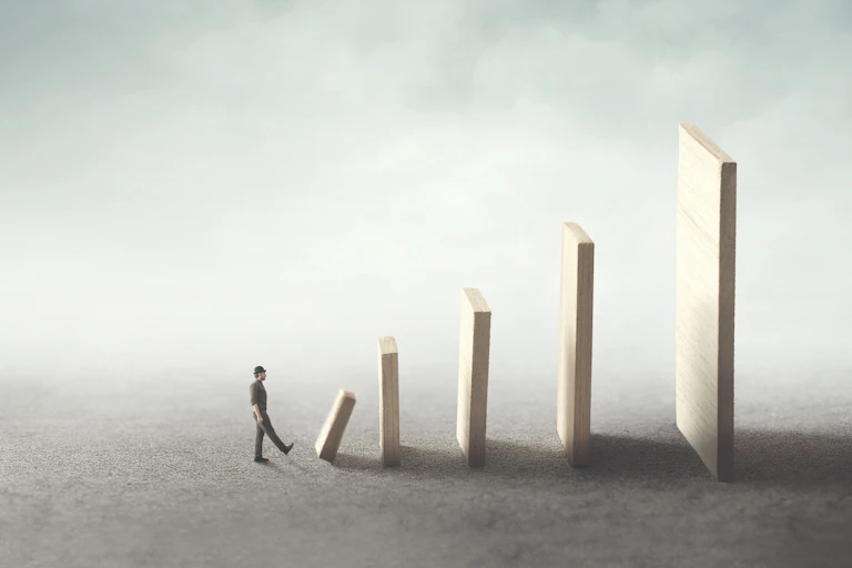 Illustration of a person kicking over a monolith, which in turn will knock over a series of increasingly larger monoliths behind it