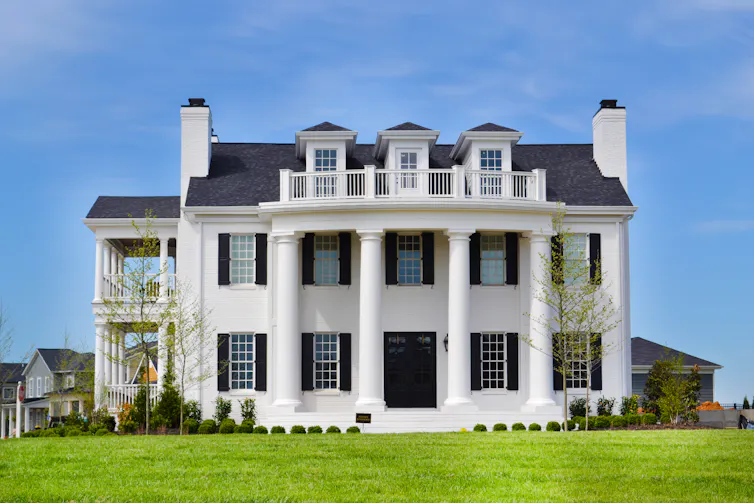 A large white mansion with dormer windows in the roof and two-storey pillars beneath.