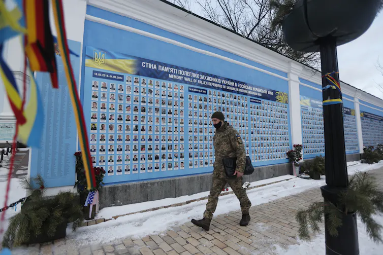 A man walks past a wall in Kyiv with the pictures of Ukrainians killed fighting separatists since 2014.