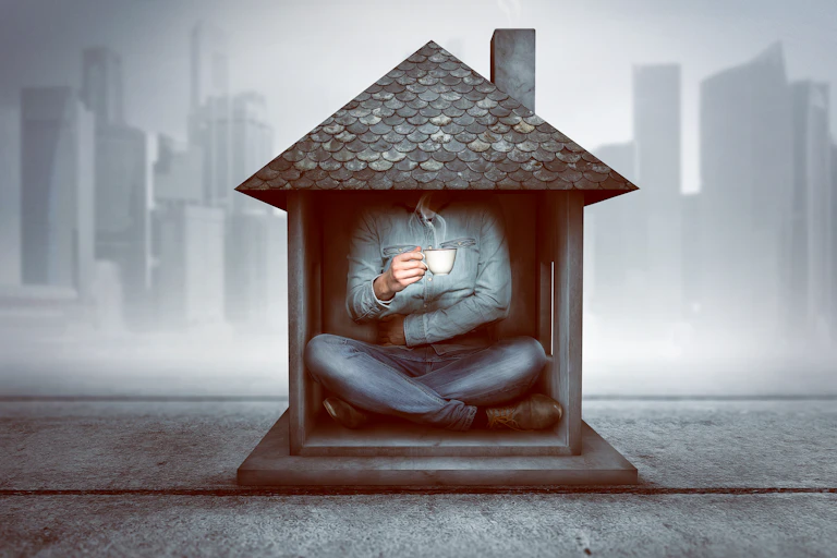 Man sitting in a tiny house with a cityscape in the background.