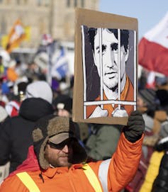 A protester holds a sign of Justin Trudeau's face behind bars.