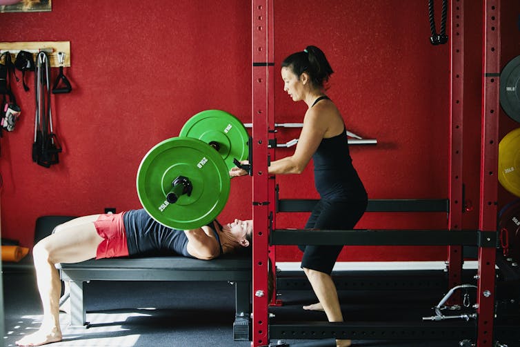 A woman spotting someone doing a bench press.