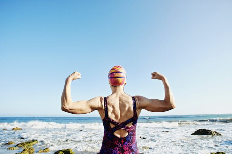 An older woman in a swimsuit flexing and showing off muscles.