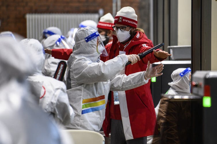 Security guards clad in full white protective gear scan Olympic competitors with batons