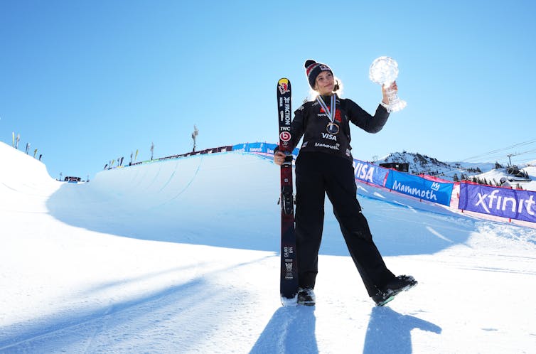 Eileen Gu, a young American-Chinese skier, holds her skis up as she stands in front of a ski slope