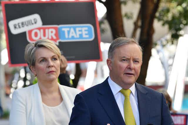 Serious-looking woman and man in front of sign reading 'Rebuild our TAFE'