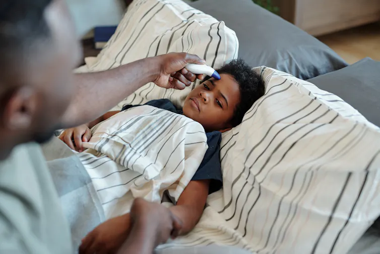 Dad takes African-Australian boy's temperature while he lays in bed.