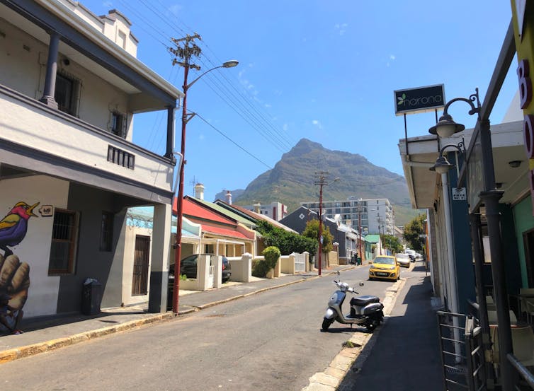 A view of a street with shops and quaint, old-fashioned houses, a mountain towering in the background.