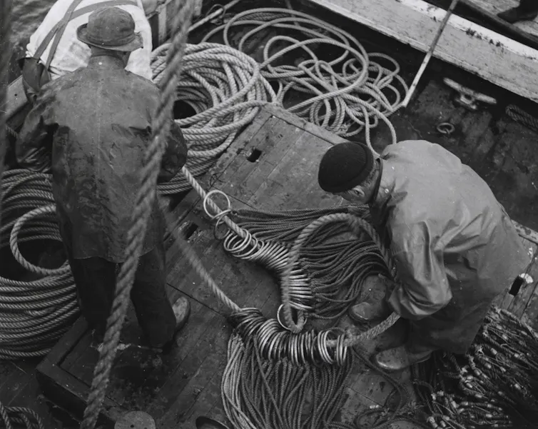 A black-and-white photo of fishermen preparing a length of rope with hundreds of metal hoops attached.