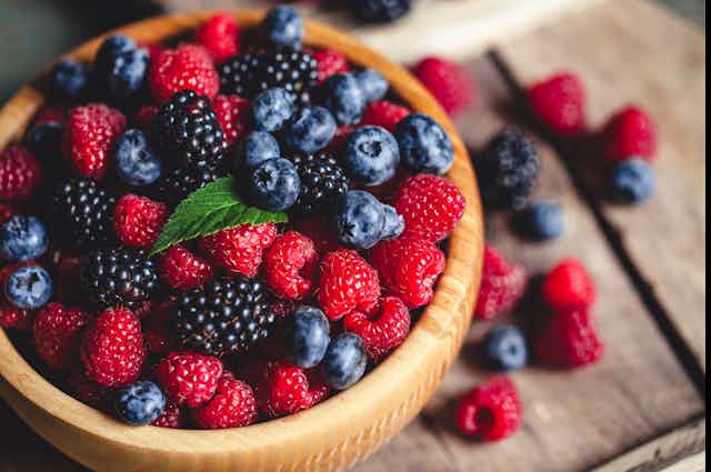 A wooden bowl full of blueberries, raspberries and blackberries.