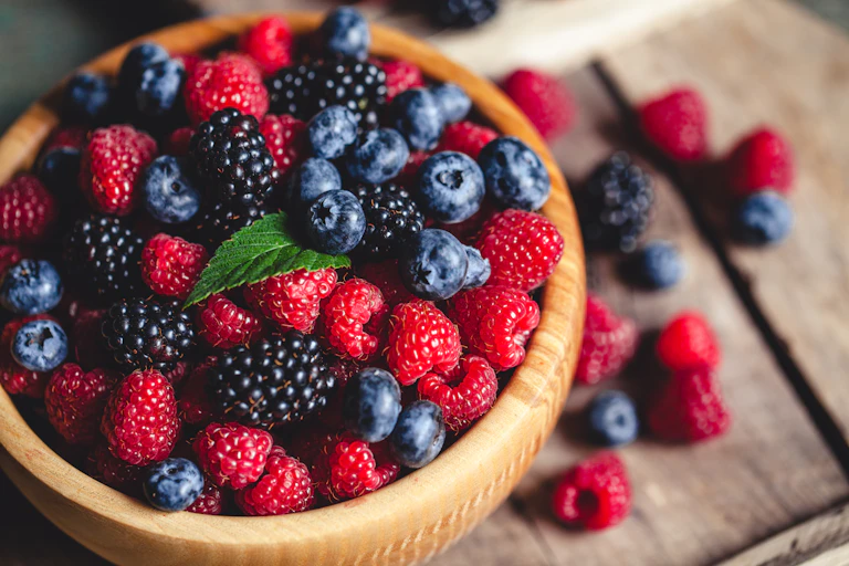 A wooden bowl full of blueberries, raspberries and blackberries.