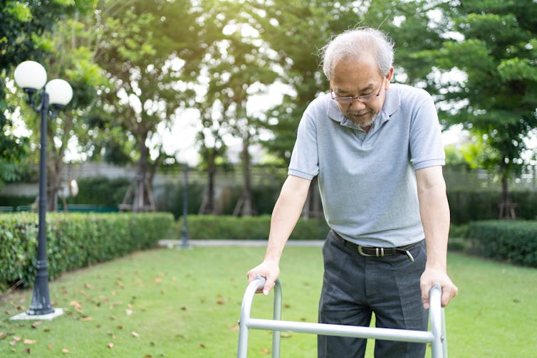 An older man using his walker to walk outside.