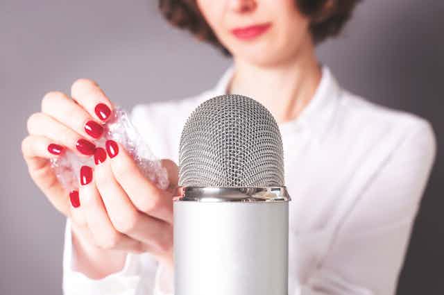 A woman holds bubble wrap next to a microphone.