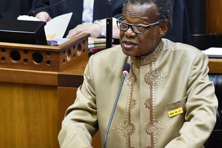 An elderly, bespectacled man speaks at a podium