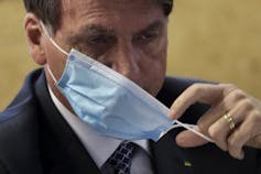 A man removes a blue surgical mask from his face.