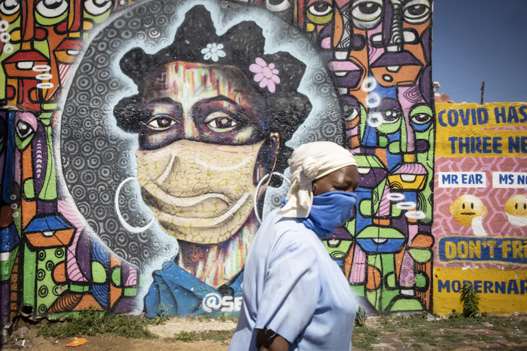 Mural of a woman in a mask with a woman in a mask walking in front of it.