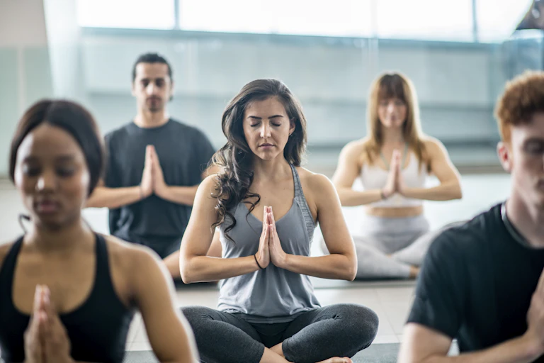 Five people doing meditation with hands folded in a prayer pose.