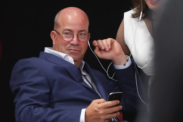 Jeff Zucker sits and stares ahead with a white earphone cord dangling from his left ear