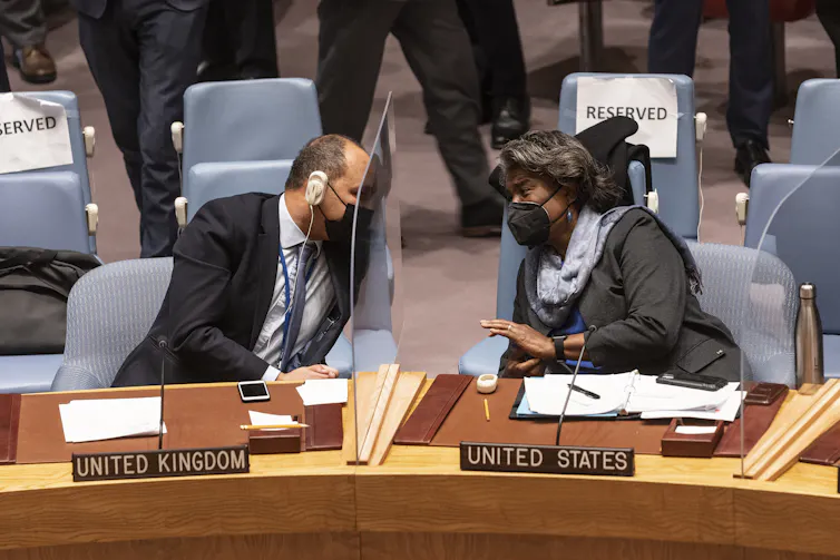El embajador del Reino Unido, James Kariuki, y la embajadora de Estados Unidos, Linda Thomas-Greenfield, se inclinan el uno hacia el otro a través de una mesa durante una reunión del Consejo de Seguridad de la ONU sobre Ucrania el 21 de enero de 2022.
