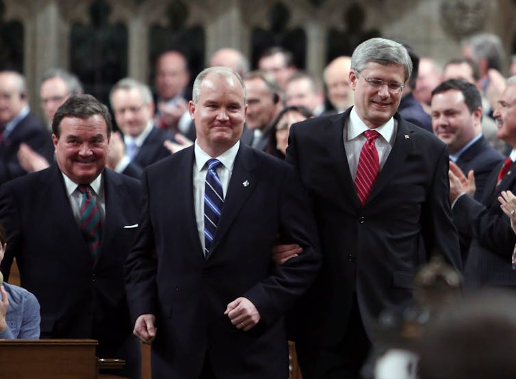 Three smiling men in blue suits in the House of Commons.
