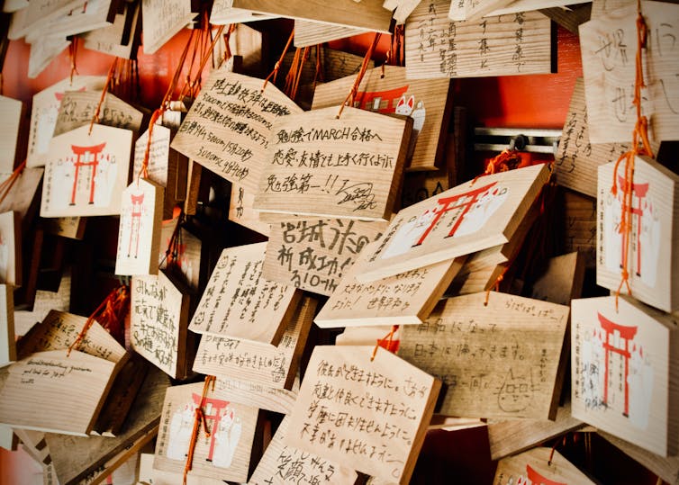 Small wooden boards hanging on red threads with messages to deities written on them.